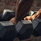 Person's hand gripping black rubber hexagon dumbbell during workout, additional dumbbells blurred in background