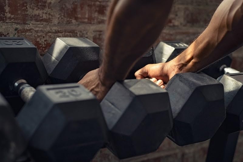 Person's hand gripping black rubber hexagon dumbbell during workout, additional dumbbells blurred in background