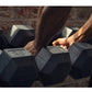 Person's hand gripping black rubber hexagonal dumbbell from a set, displayed on gym floor with brick wall background