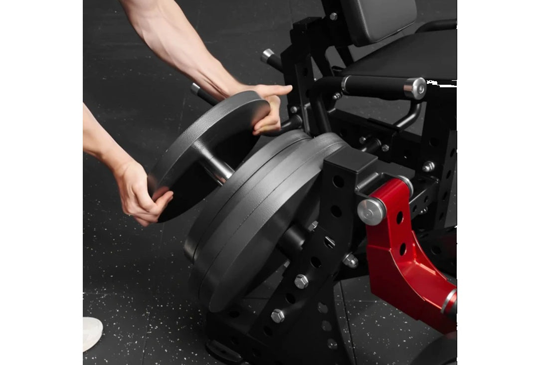 Model demonstrating black plate-loaded leg extension machine with red frame and adjustable seat, hands gripping padded lever