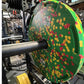Warrior Fleck Easy-Grip green rubber bumper plate with red and yellow flecks, mounted on barbell in gym setting