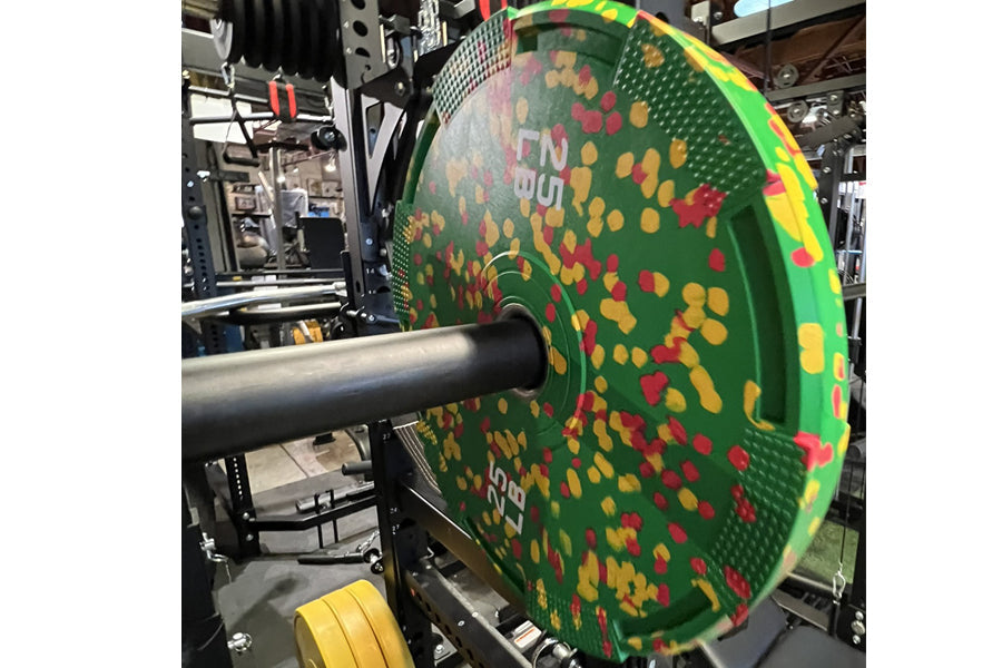 Warrior Fleck Easy-Grip green rubber bumper plate with red and yellow flecks, mounted on barbell in gym setting