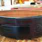 Brown leather belt with black buckle and embossed logo, flat lay on workbench
