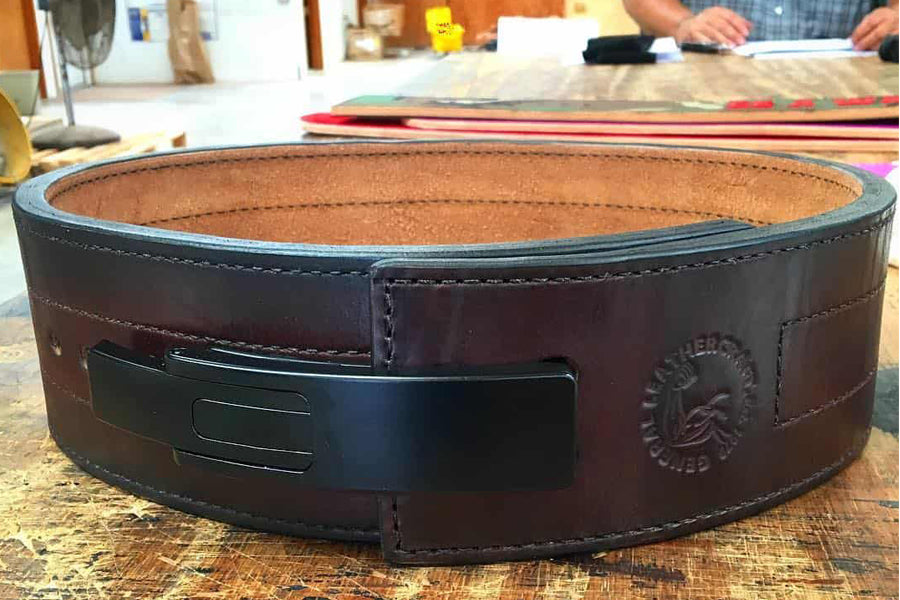 Brown leather belt with black buckle and embossed logo, flat lay on workbench