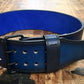 Black leather power belt with blue interior, metal buckle, and double-row metal grommets, flat lay on wooden surface