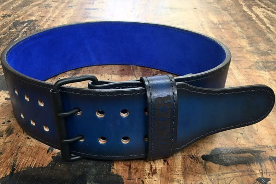Black leather power belt with blue interior, metal buckle, and double-row metal grommets, flat lay on wooden surface