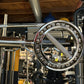 Chrome Olympic curl bar with studded collar ring and textured grip, mounted on weight rack