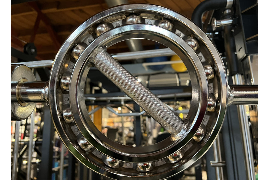 Polished steel Olympic curl bar with textured grip and ball bearing collar, displayed in workshop setting