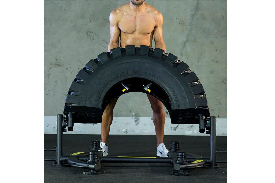 Shirtless male model performing tire flip exercise with large black rubber tire on Warrior Tire Flip 180 machine