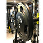 Black rubber Olympic weight plate with grip handles, marked 45 pounds, displayed in gym setting