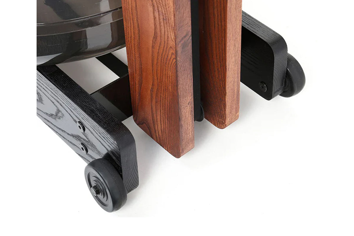 WaterRower Club rowing machine detail showing wooden frame with cherry finish legs and black rubber caster wheels on white ba