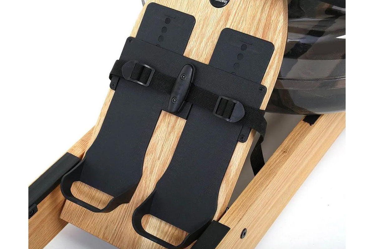 Black foot pedals with nylon straps and metal buckles on natural oak rowing machine footplate, flat lay view