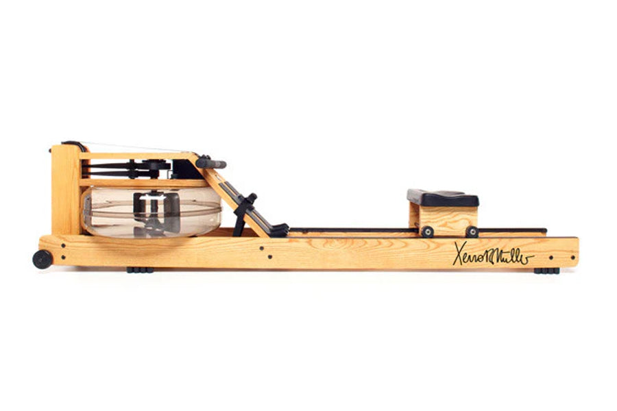 Xeno Muller Signature Edition wooden rowing machine with clear water tank, black hardware, and wheels on white background