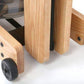 Natural wood rowing machine with black wheels and metal hardware, detail of wooden leg and caster wheel on white background