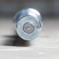 Silver metal Olympic barbell end cap with circular grip pattern and engraved text on concrete surface