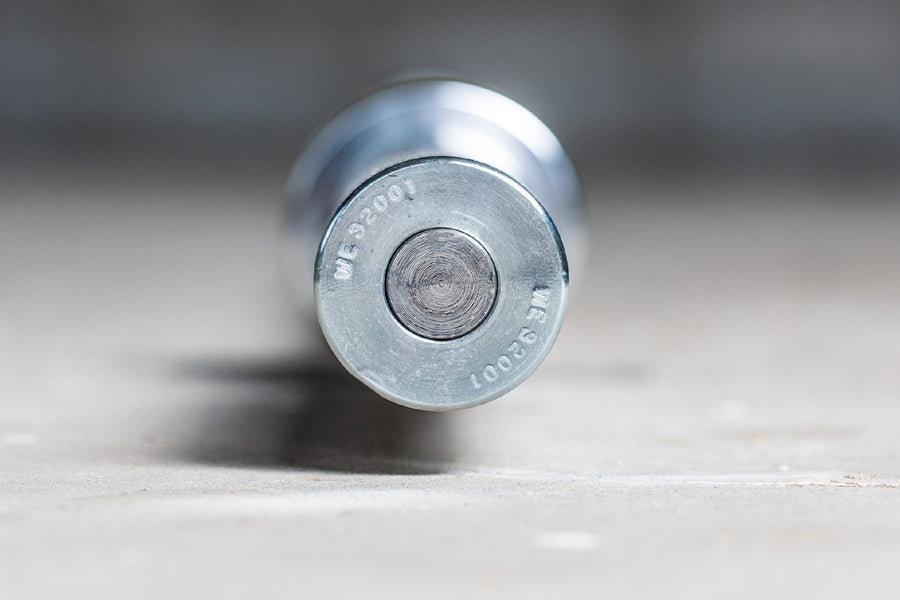Silver metal Olympic barbell end cap with circular grip pattern and engraved text on concrete surface